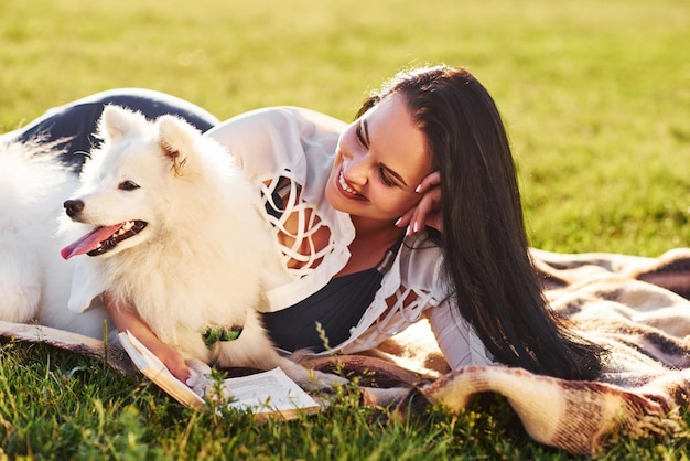 Woman having a rest on the ground of field with her cute white dog