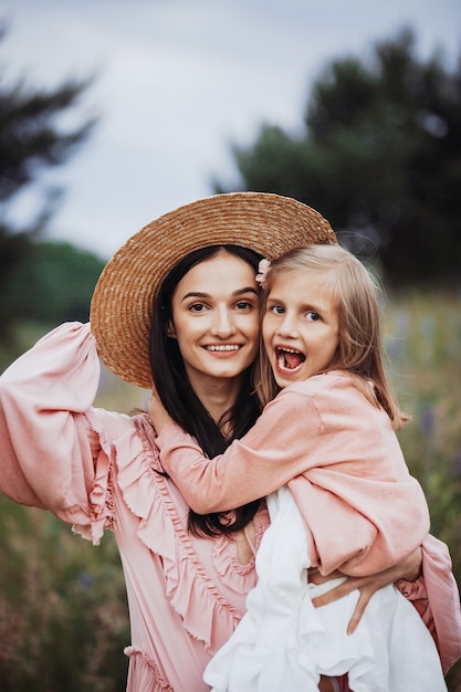 Photo woman in hay hat holds little girl on her arms standing on the field