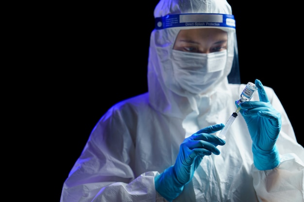 Woman in hazmat suit with vaccine and syringe injection for prevention, immunization and treatment from corona virus infection.