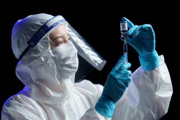 Woman in hazmat suit with vaccine and syringe injection for prevention, immunization and treatment from corona virus infection.