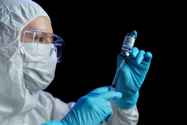 Woman in hazmat suit with vaccine and syringe injection