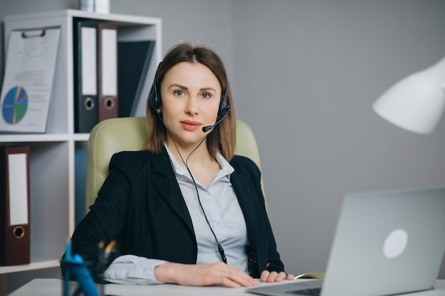 La donna in cuffie che tengono la conversazione di carta del rapporto finanziario alla webcam fa la video chiamata in ufficio