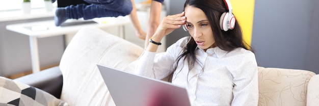 Woman in headphones and laptop sits on sofa next to child pampering