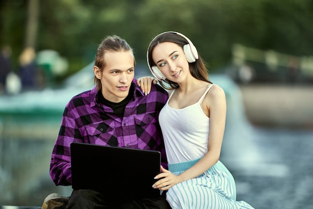 Woman in headphones and man with laptop has elearning outdoors