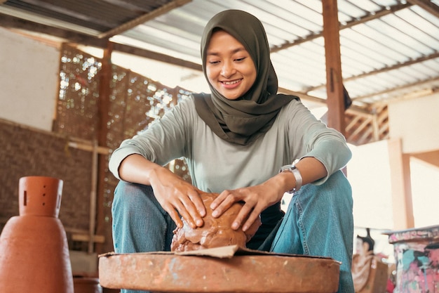 Woman in headscarf sitting relaxed holding wet clay on\
wheels