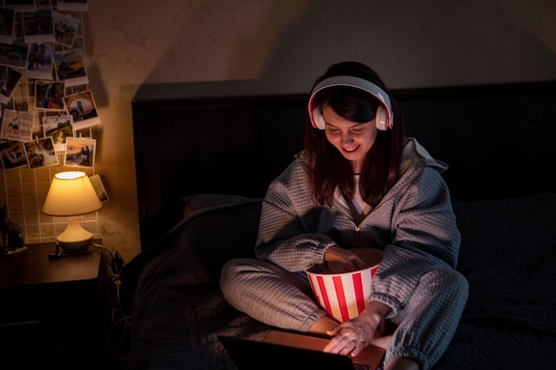 Woman in headset sitting on the bed eating pop corn watching movie