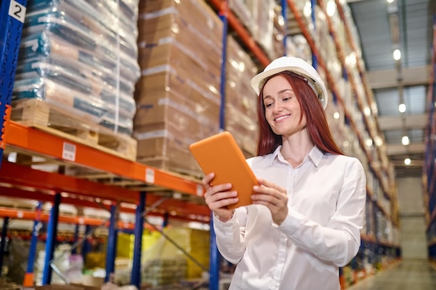 Woman in helmet looking at tablet at warehouse