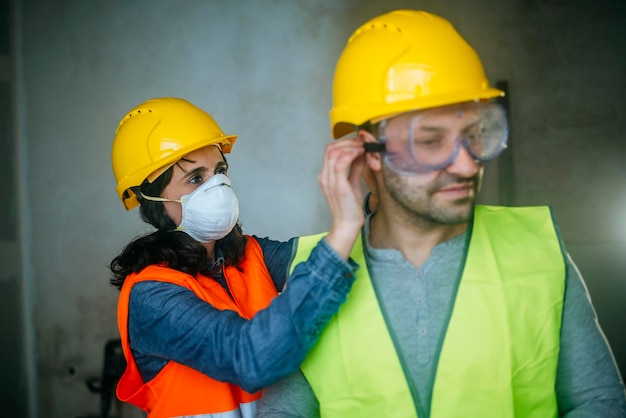 Woman helping man putting on safety glasses on a construction site