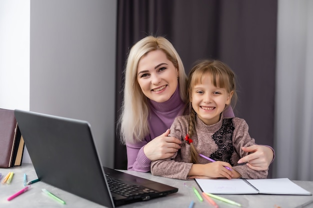 Woman helping young girl with laptop do homework in dining room