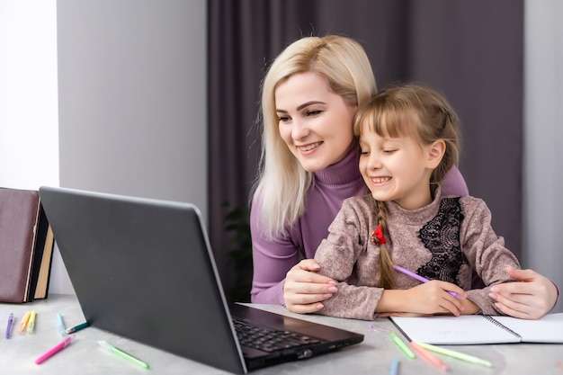 Woman helping young girl with laptop do homework in dining room