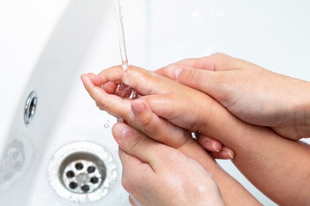 Photo woman helps children wash hands under the tap close-up