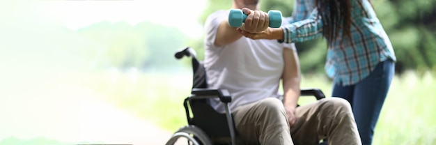 Woman helps man in wheelchair to do exercises with dumbbells