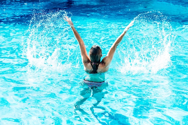 Woman on her back in a pool raised water with arms in paradisiacal water