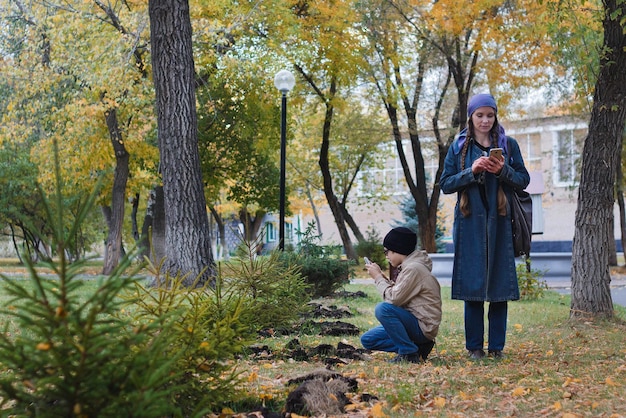 秋に公園の小さな木の携帯電話で写真を撮る女性と彼女の子供