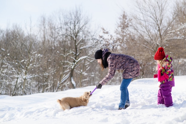 Woman and her daugther play with dog in snow forest