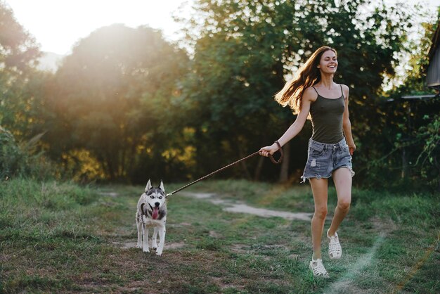 Photo woman and her husky dog happily running through the grass in nature in the park smile with teeth fall walk with pet traveling with a dog friend high quality photo