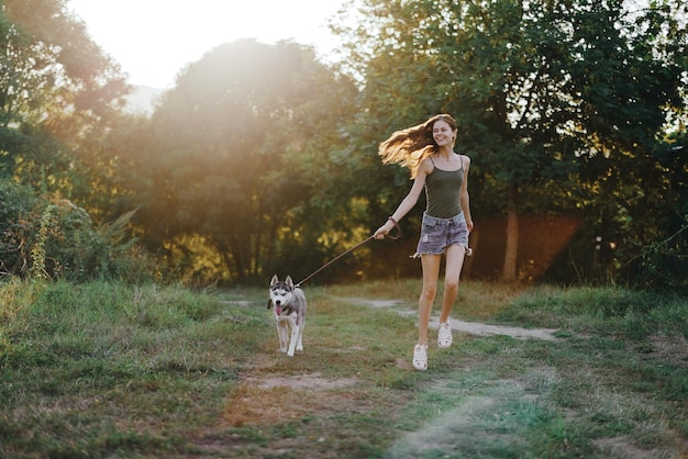 Woman and her husky dog happily running through the grass in nature in the park smile with teeth fall walk with pet traveling with a dog friend