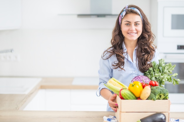 Женщина на кухне с деревянным ящиком, полным органических овощей.