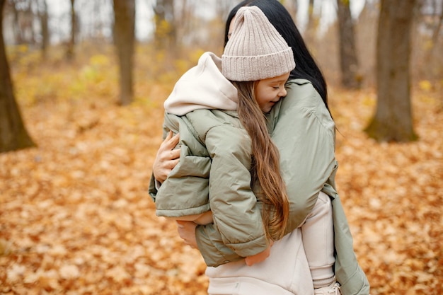 Woman and her little girl playing in autumn forest and laughing Brunette man hugging her daughter Family wearing green coats