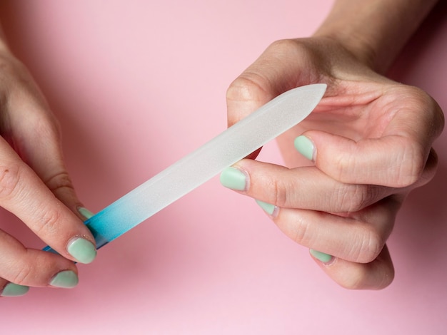 A woman herself is filing her nails with a nail file on her hand on a pink background. Hand nail care at home. Beauty and Health