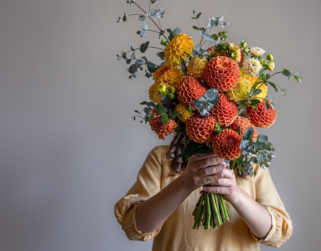 Woman hid her face with a bouquet of yellow and orange chrysanthemums, gray background, copy space.