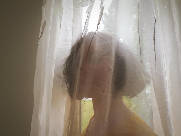 Photo woman hiding behind curtain at home