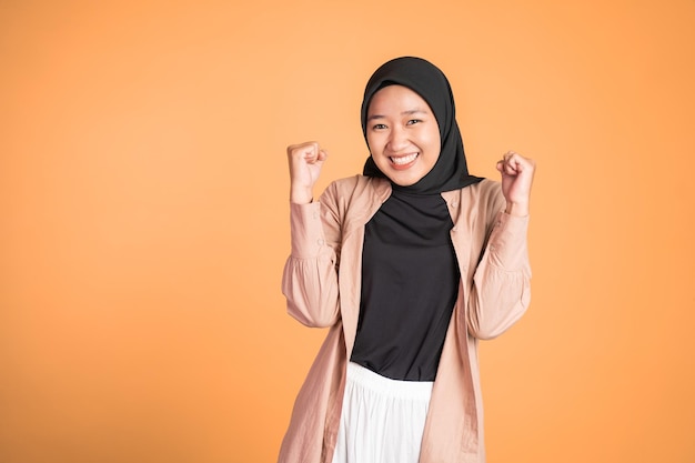 Woman in hijab clenching hands while celebrating success