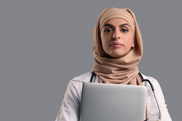 Foto donna in hijab e camice da laboratorio con un computer portatile