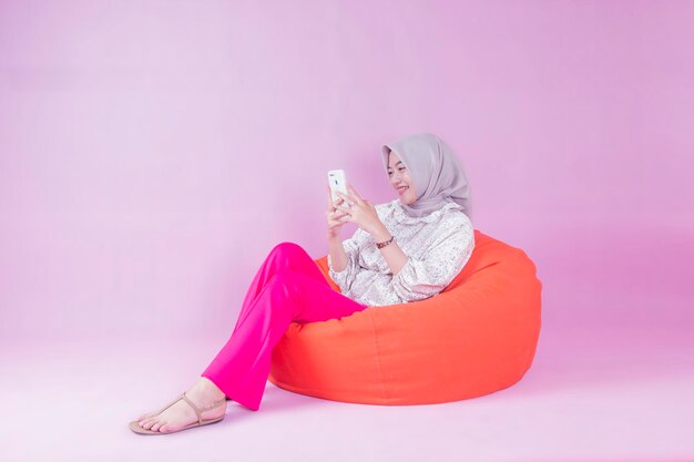 Женщина в хиджабе сидит на мешочке с фасолью и смотрит в свой телефон.