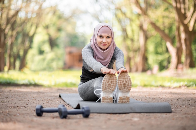 Женщина в хиджабе растягивает тело в летнем парке