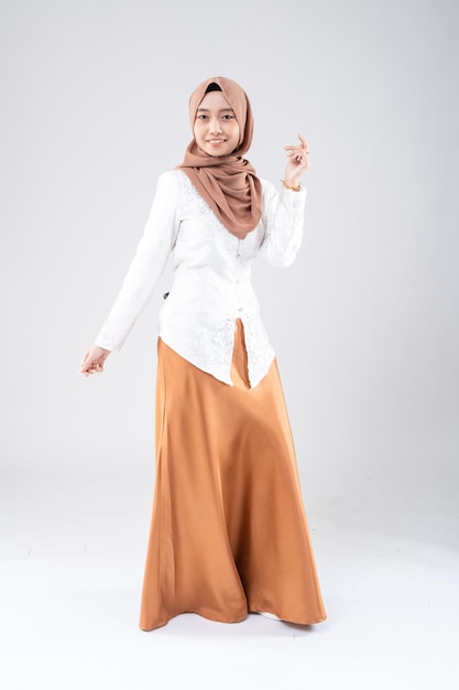 A woman in a hijab and a white shirt is standing in front of a white background.