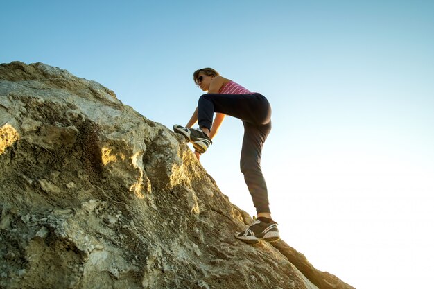 Woman hiker climbing a steep big rock