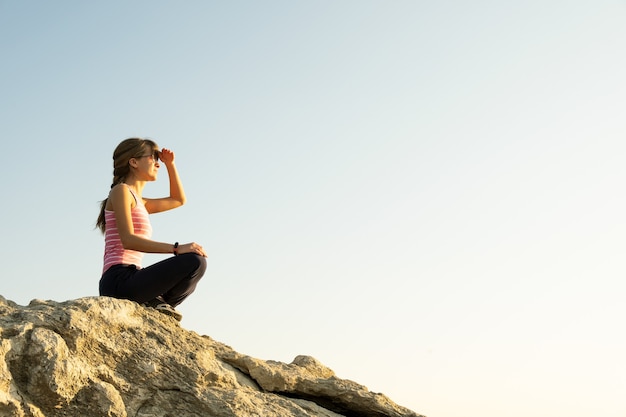 Woman hiker sitting on a steep big rock enjoying warm summer day