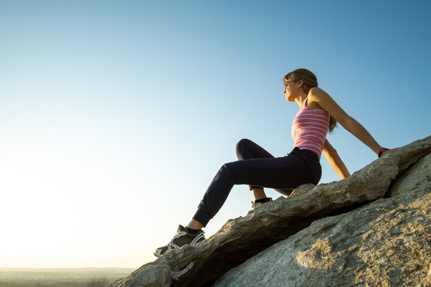 Woman hiker sitting on a steep big rock enjoying warm summer day