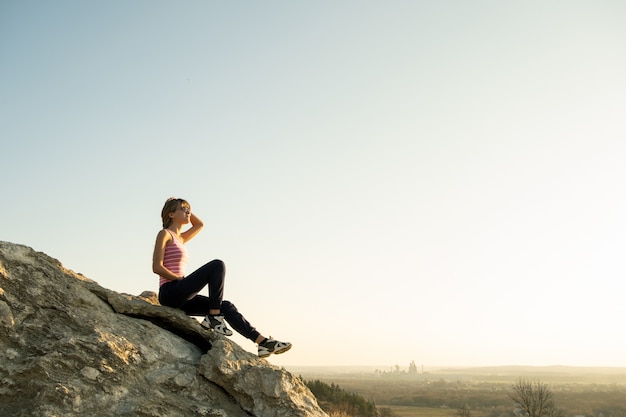 Woman hiker sitting on a steep big rock enjoying warm summer day