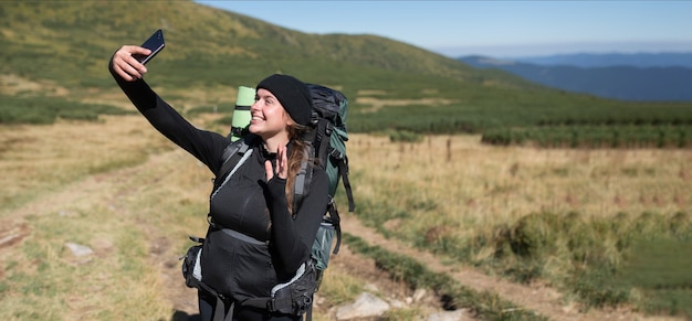 Foto escursionista donna si trova sulla cima della montagna, tiene un telefono in mano e fa una videochiamata