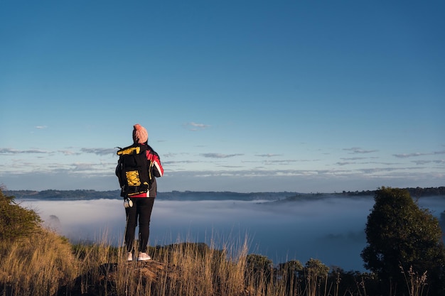 Woman hiker with backpack enjoying the foggy scenery at the top of the mountain.