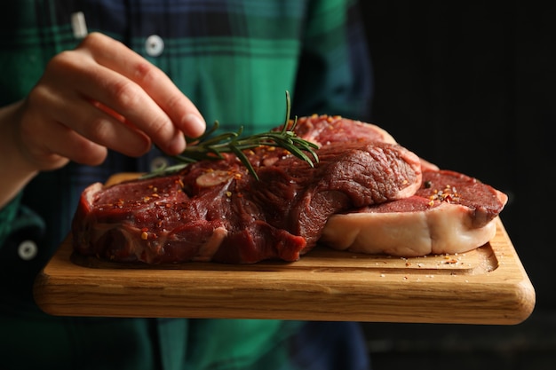 Woman hold board with raw steak meat, close up