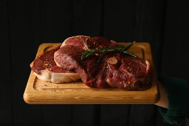 Woman hold board with raw steak meat on wooden