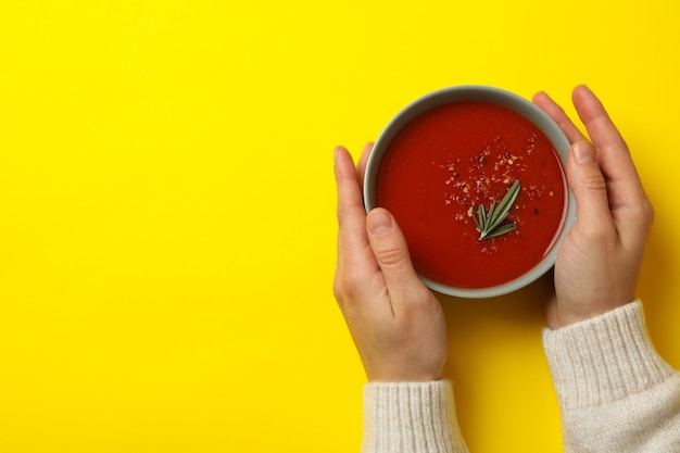 Woman hold bowl of tasty tomato soup on yellow