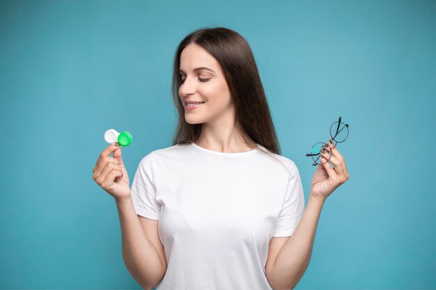 woman hold contact lenses and glasses in hands. concept of choice of vision protection