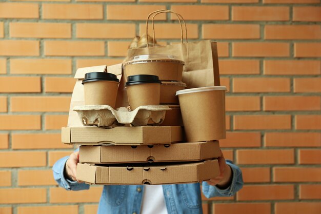 Woman hold delivery containers for takeaway food on brick wall surface