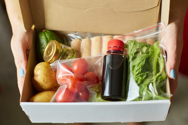 Foto la donna tiene in mano il kit pasto della scatola del cibo di ingredienti freschi ordinati da un'azienda di kit pasto, consegnati, cucinati a casa.