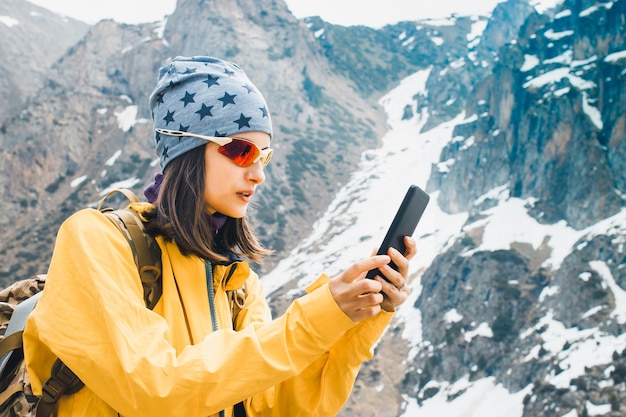 Woman hold in hands mobile phone planning trip in rock snow mountain