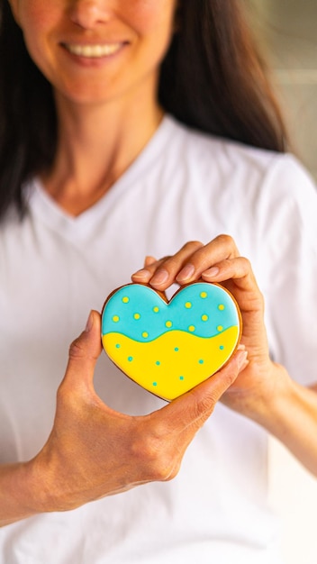 Woman hold heart shape gingerbread cookie with ukrainian flag colors in hands