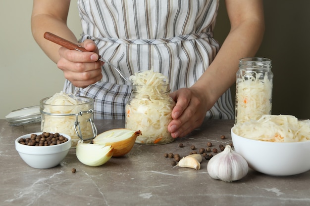 Woman hold jar with sauerkraut on gray textured table with ingredients