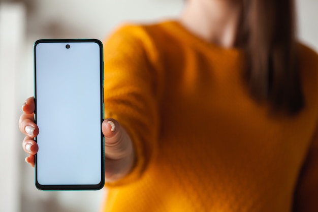 Woman hold mobile phone screen mockup in hands in orange sweater