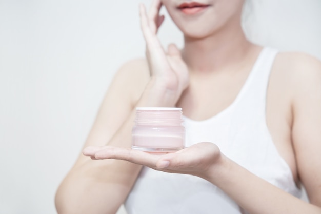 Woman hold a moisturizer cream in her hand and applying the cream on her face