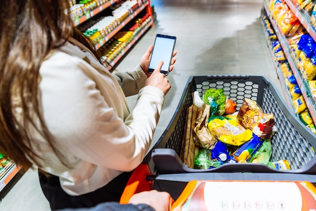 食料品の買い物をしている間、女性は白い画面で電話を保持します