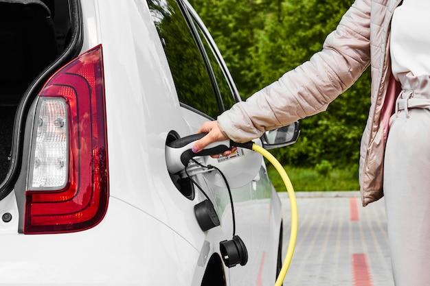 Woman hold power supply plugged into an electric car at public charging station outdoors.